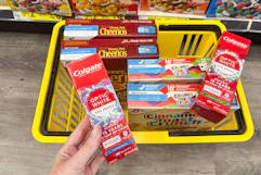 hand holding up colgate toothpaste over yellow shopping basket