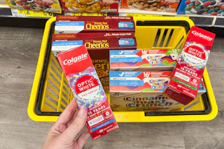 hand holding up colgate toothpaste over yellow shopping basket
