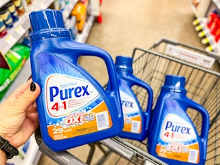 hand holding bottle of laundry detergent in front of shopping cart with detergent
