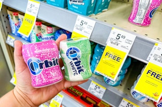 person holding 2 packs of orbit gum by the shelf