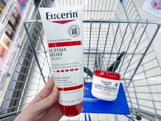 An Eucerin Eczema relief cream held out by hand in front of a Eucerin Original Healing Lotion sitting in a store cart.