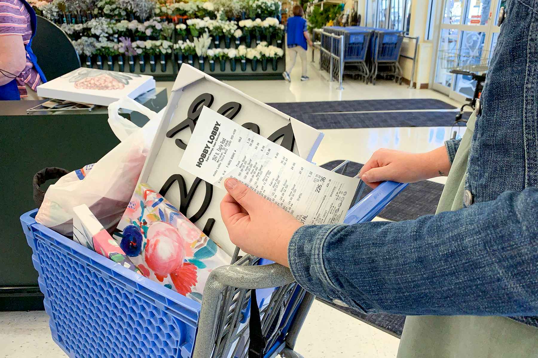 A woman holding a receipt in front of a basket filled with products at the return register.