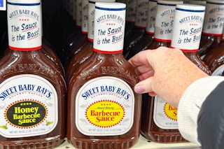 hand reaching for a bottle of sweet baby ray's barbecue sauce