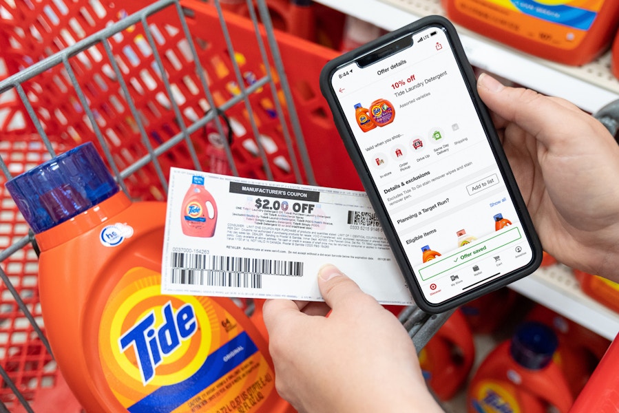 A person's hands holding a cell phone displaying 10% off Tide laundry detergent on the target circle app and a $2 off manufacture coupon,...