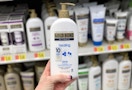 A hand holding a bottle of Gold Bond lotion in a store aisle.