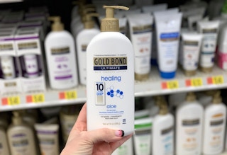 A hand holding a bottle of Gold Bond lotion in a store aisle.