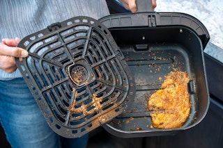 A person holding up a filthy air fryer pan and tray.