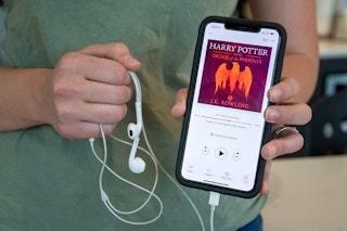 A woman holding an iPhone and head phones with Harry Potter and the Order of the Phoenix from audible on the screen.