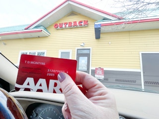 a person holding an aarp card while in a card outside outback steak house curbside 