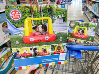 A Little tikes cozy cool canopy pool box held out by hand in front of a store cart with another cozy cool canopy pool sitting in it.